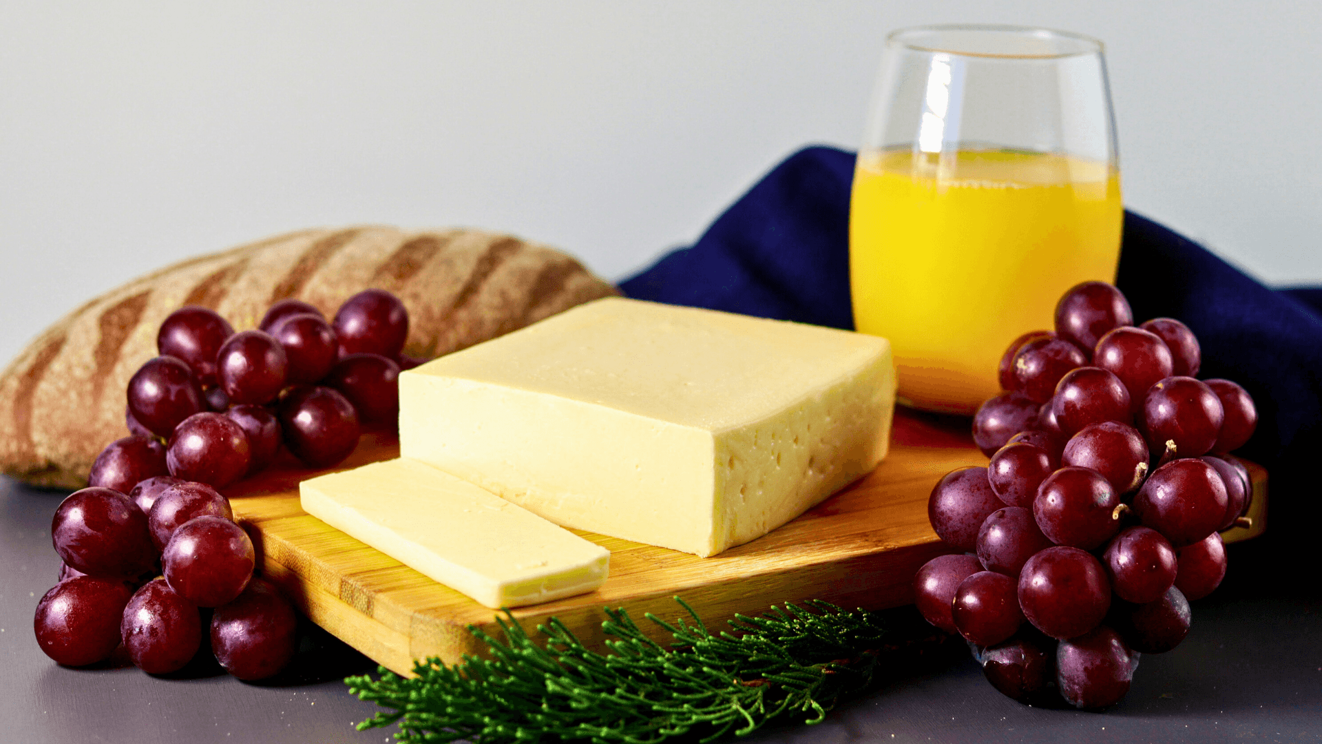 Queijo mussarela fatiado na tábua com uvas e suco de laranja