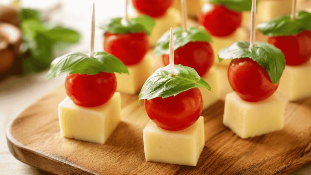 Espetinhos com tomate cereja, folhas de manjericão e cubos de queijo mussarela.