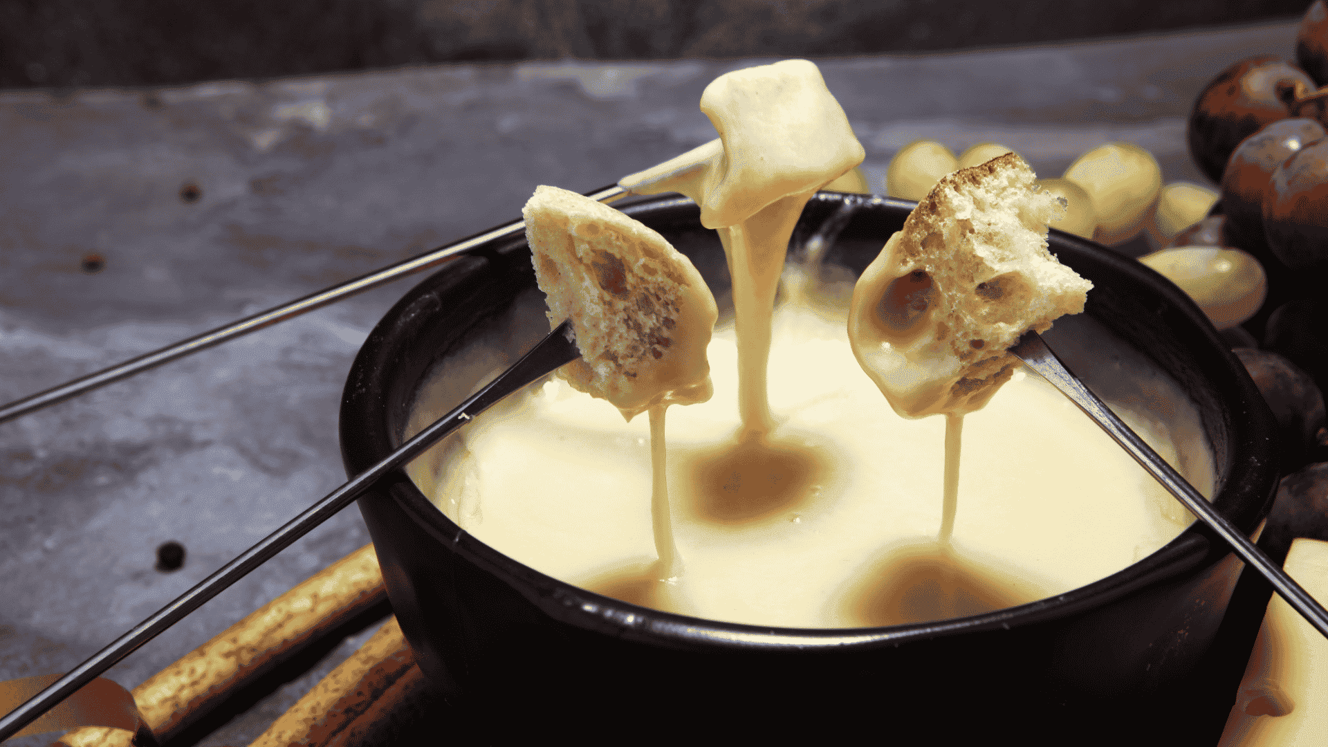 Fotos para o Blog Litoral Laticínios (1) Fondue de queijo servido com pedaços de pão e uvas sobre a mesa.