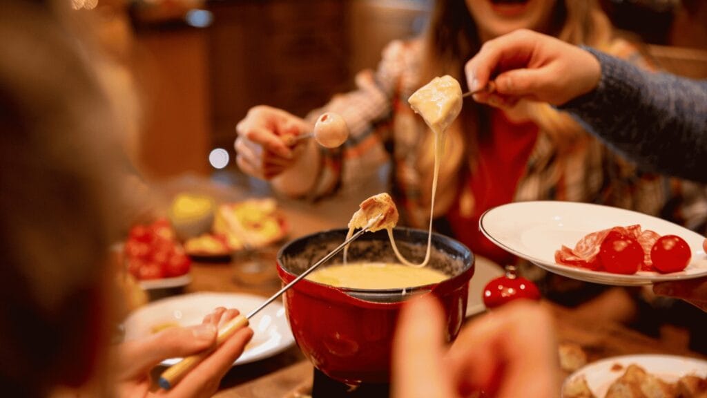 Uma família compartilhando um fondue de queijo cremoso com pães e acompanhamentos.